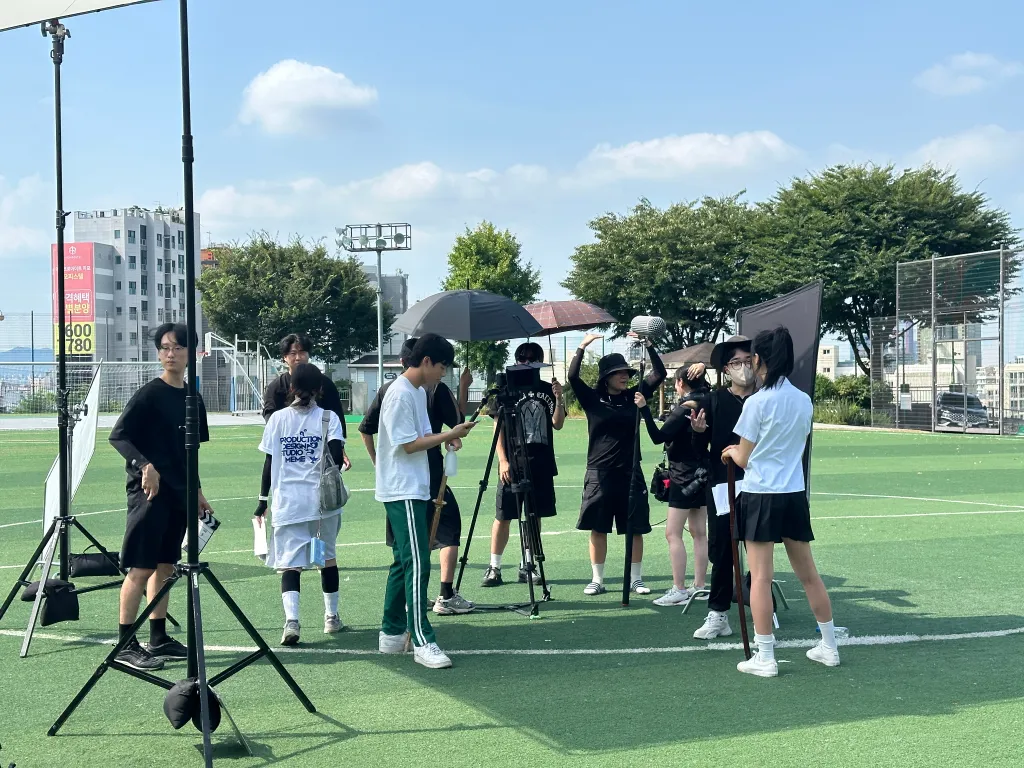 인조잔디가 깔린 환일고등학교 운동장 한가운데 집결해서 촬영하고 있는 배우와 스태프들의 모습.