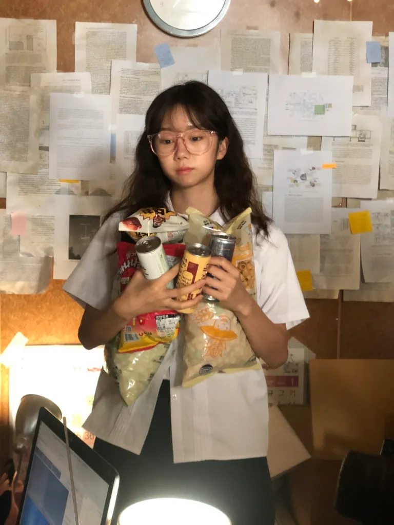 젤리 역할의 배우 신시예가 촬영 장소인 컨테이너 내부에 분홍 안경을 쓰고 과자와 음료수를 품에 잔뜩 끌어안은 모습.